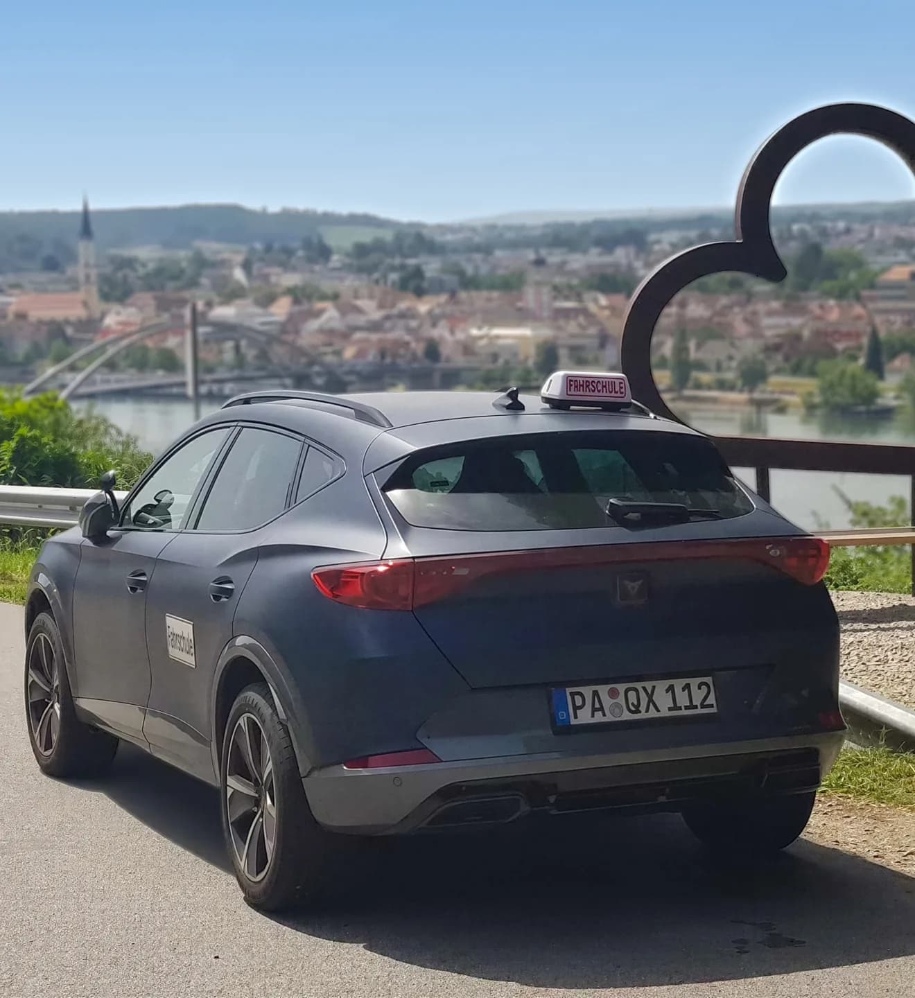 Fahrschulauto von VilsDrive neben der Herz-Skulptur am Donauufer, dahinter die Altstadt von Vilshofen